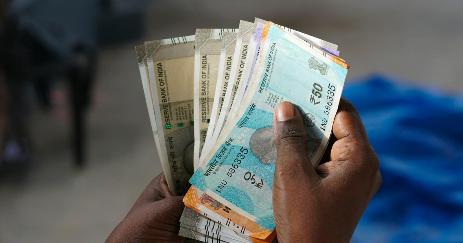 A hand holding a fan of Indian rupee notes