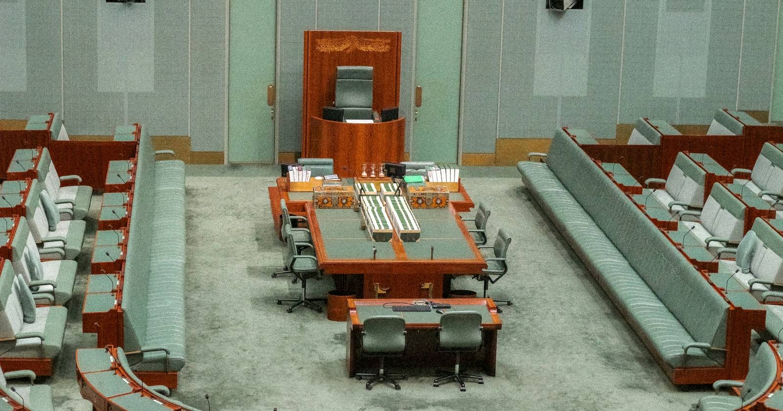 An empty parliamentary chamber, tiered seating around a central table, the session over