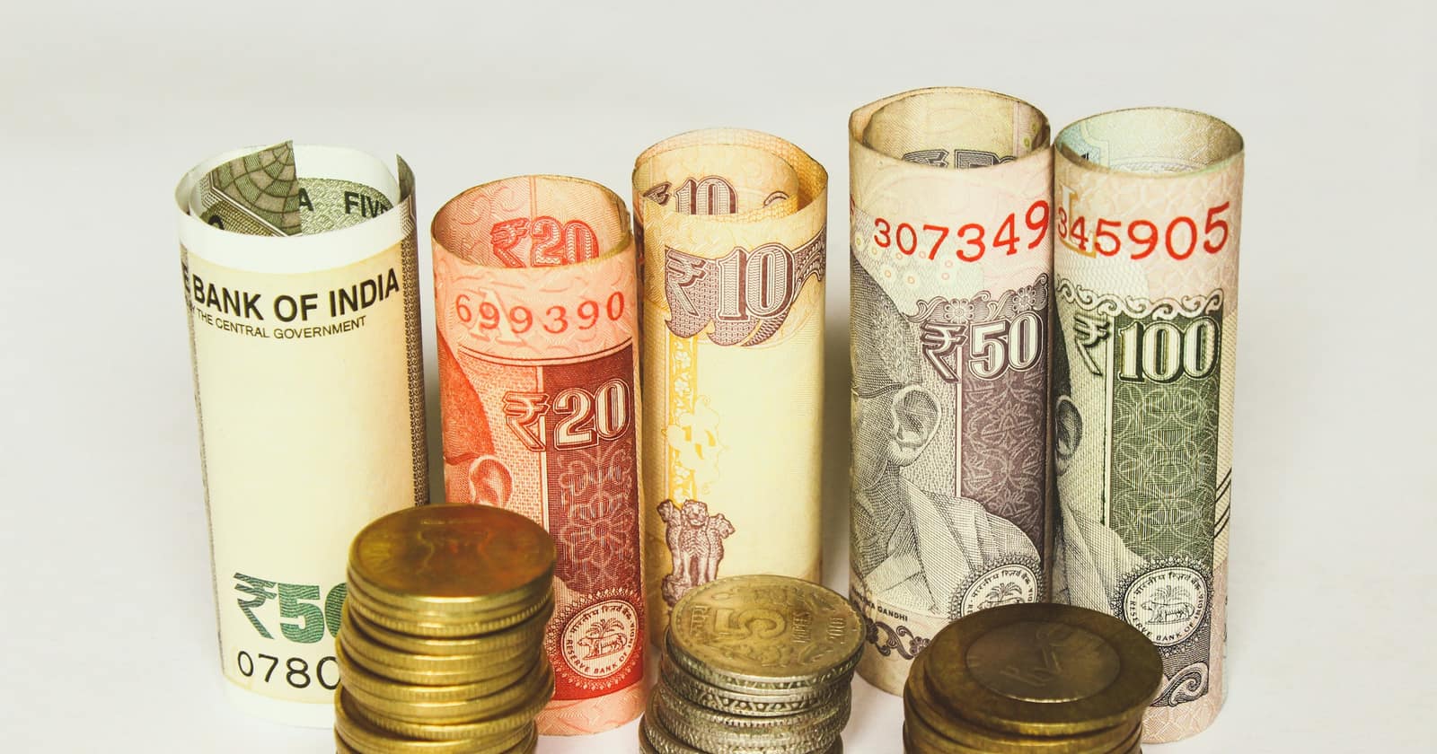 Rolled Indian rupee notes standing behind three stacks of rupee coins