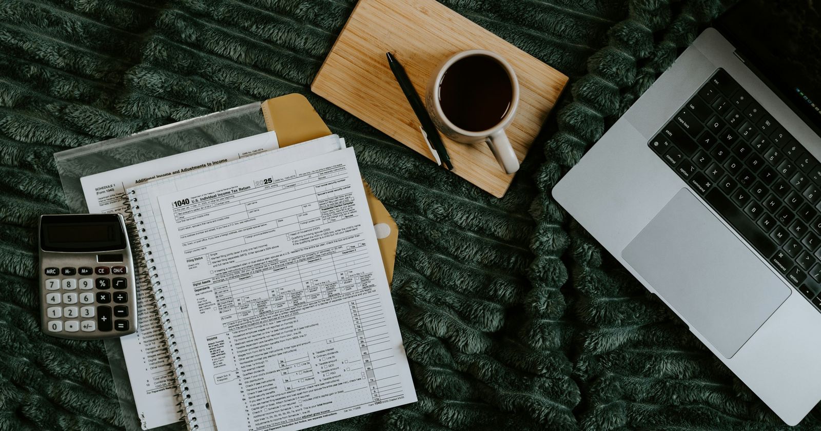 A laptop, printed statements, a calculator and a cup of coffee