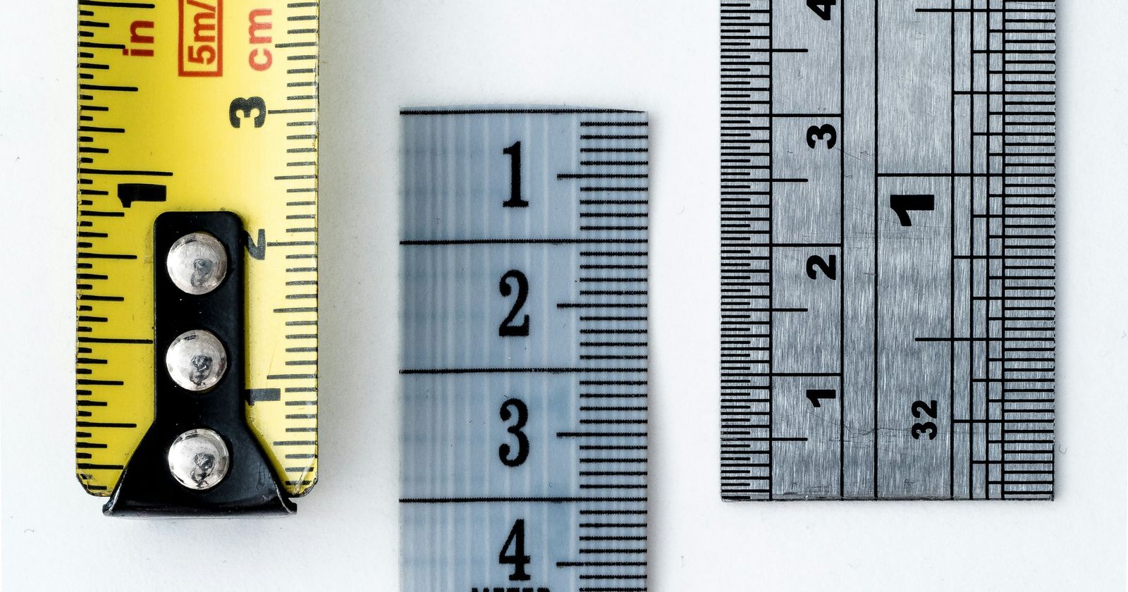 A tape measure and two metal rulers laid side by side on white