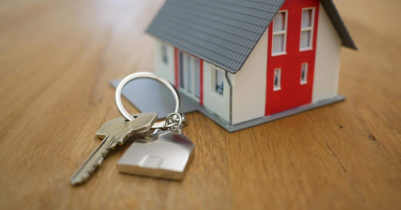 A small wooden model of a house with a red door beside a set of keys on a table