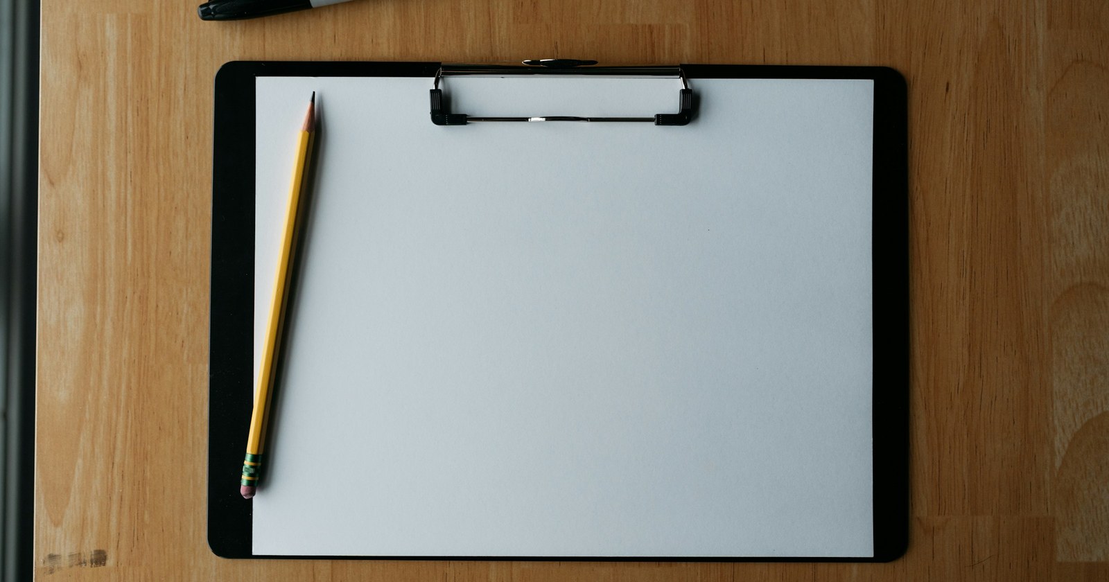 A clipboard with a pencil and a pen resting on a wooden surface