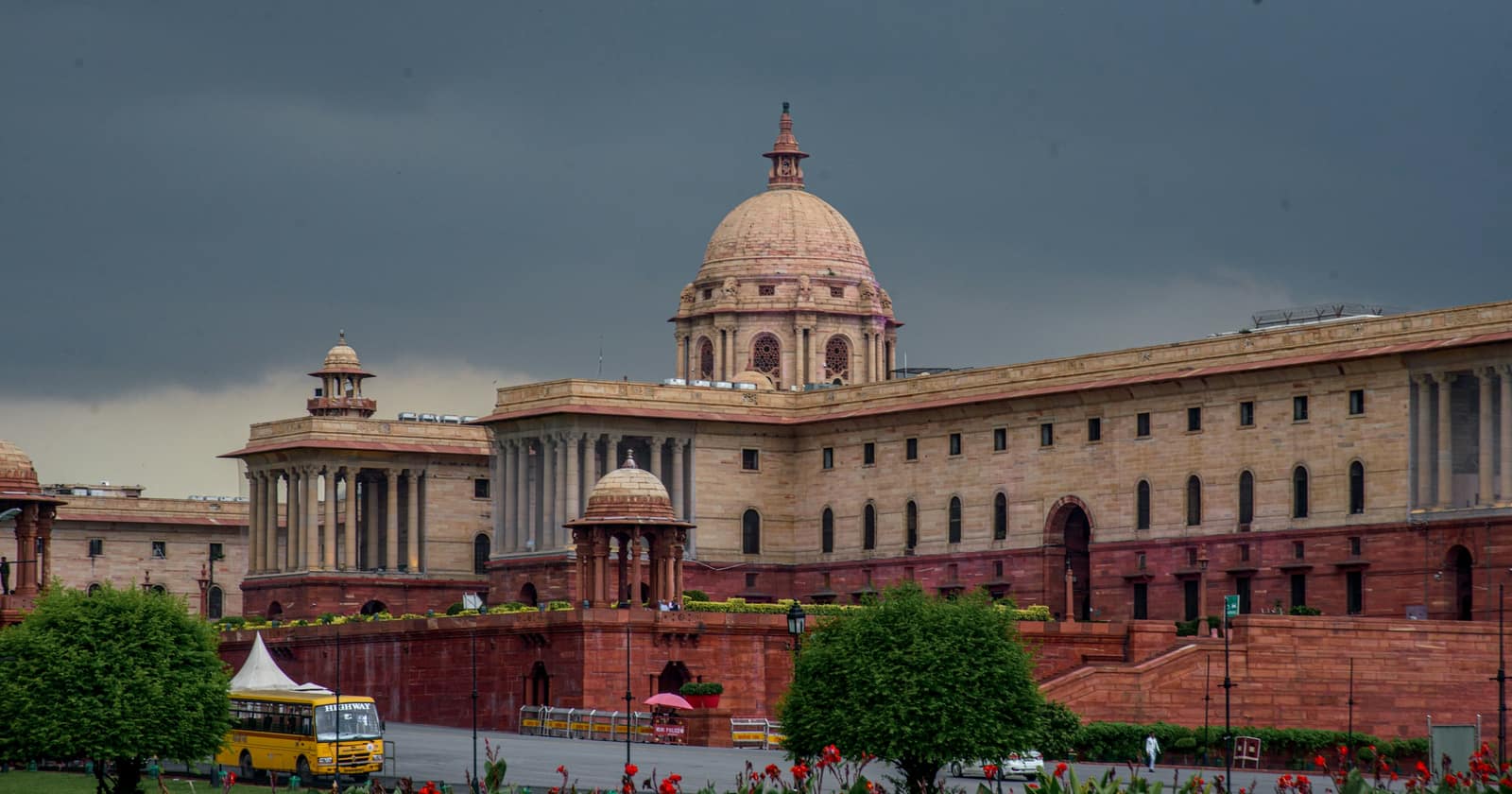 A domed red sandstone government building on Raisina Hill in New Delhi under a dark monsoon sky