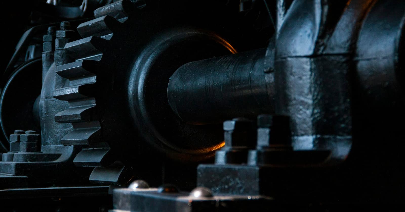 Heavy black gears and a drive shaft of an old machine, lit from one side in the dark