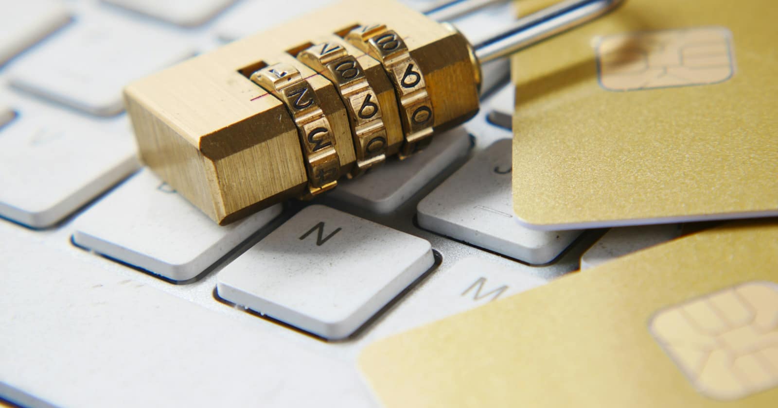 A brass combination padlock resting on a white keyboard beside two chip cards