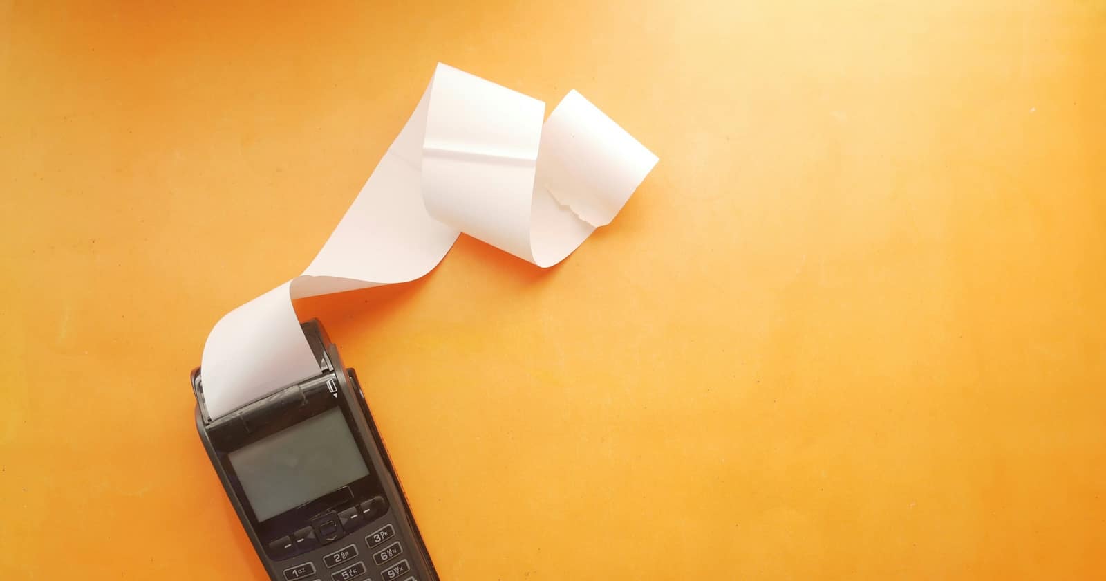 A card payment terminal printing a long paper receipt on an orange surface