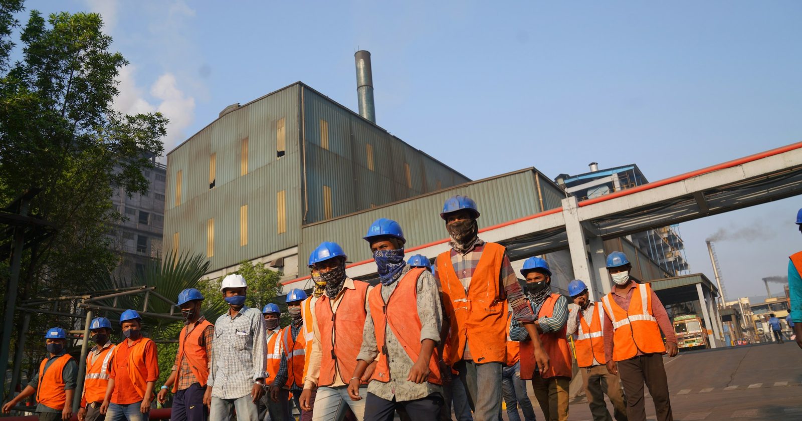 Workers in orange high-visibility vests and helmets gathered at a site, the workforce the ceiling reaches