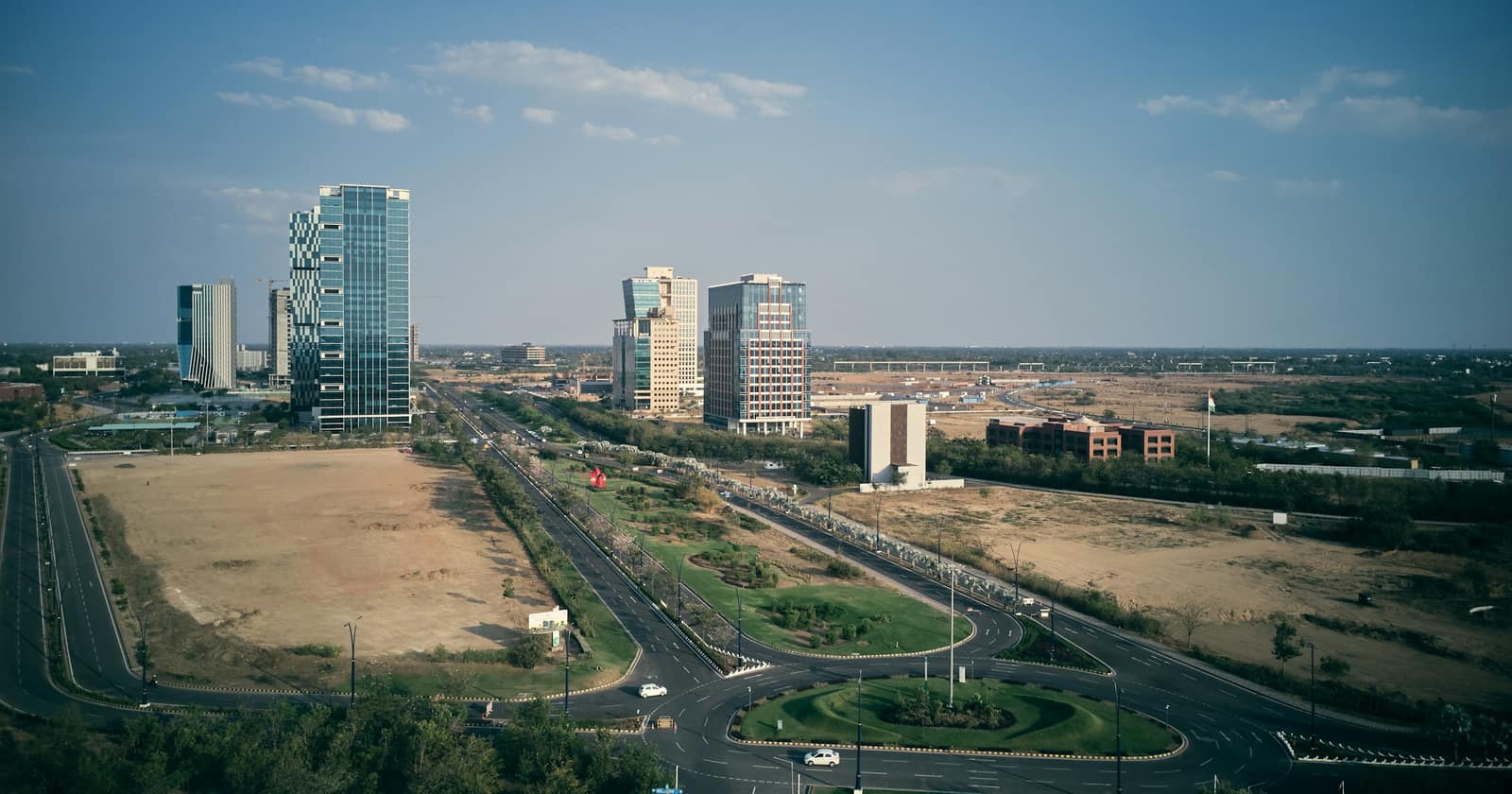 The glass towers of GIFT City rising from open land beside a curving road, Gandhinagar, Gujarat