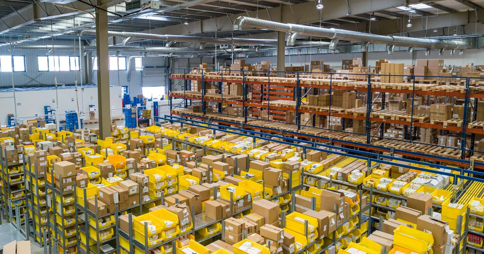A warehouse floor of shelving and yellow crates filled with cartons, seen from above