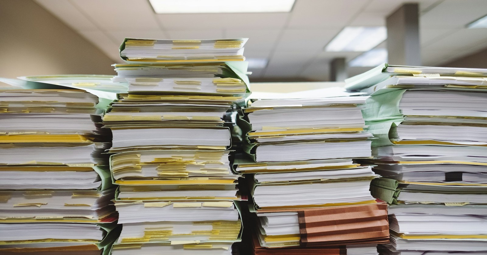 Tall stacks of paper files and folders on desks in an office