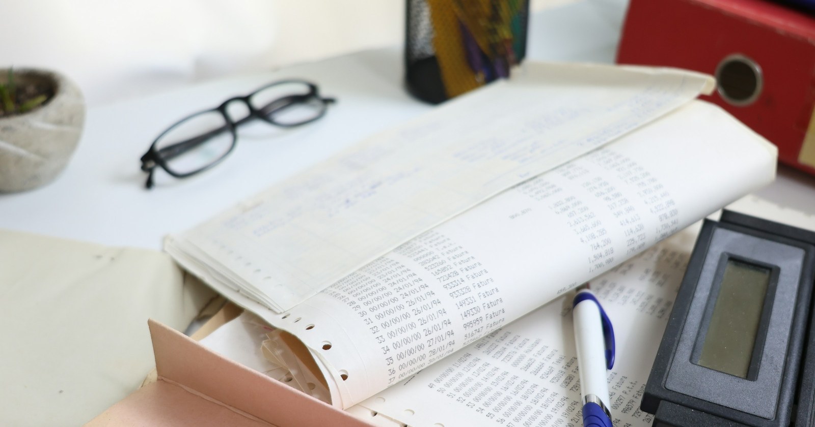 A desk with papers, spectacles, a calculator and office supplies