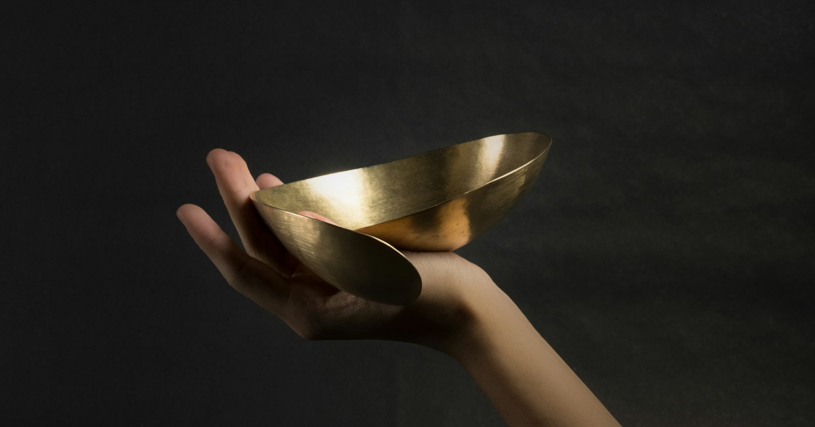 A hand holding a small curved brass bowl