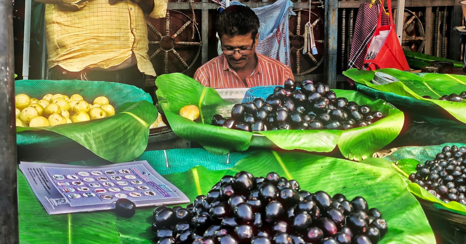 A market vendor behind heaps of jamun fruit and guavas laid out on banana leaves