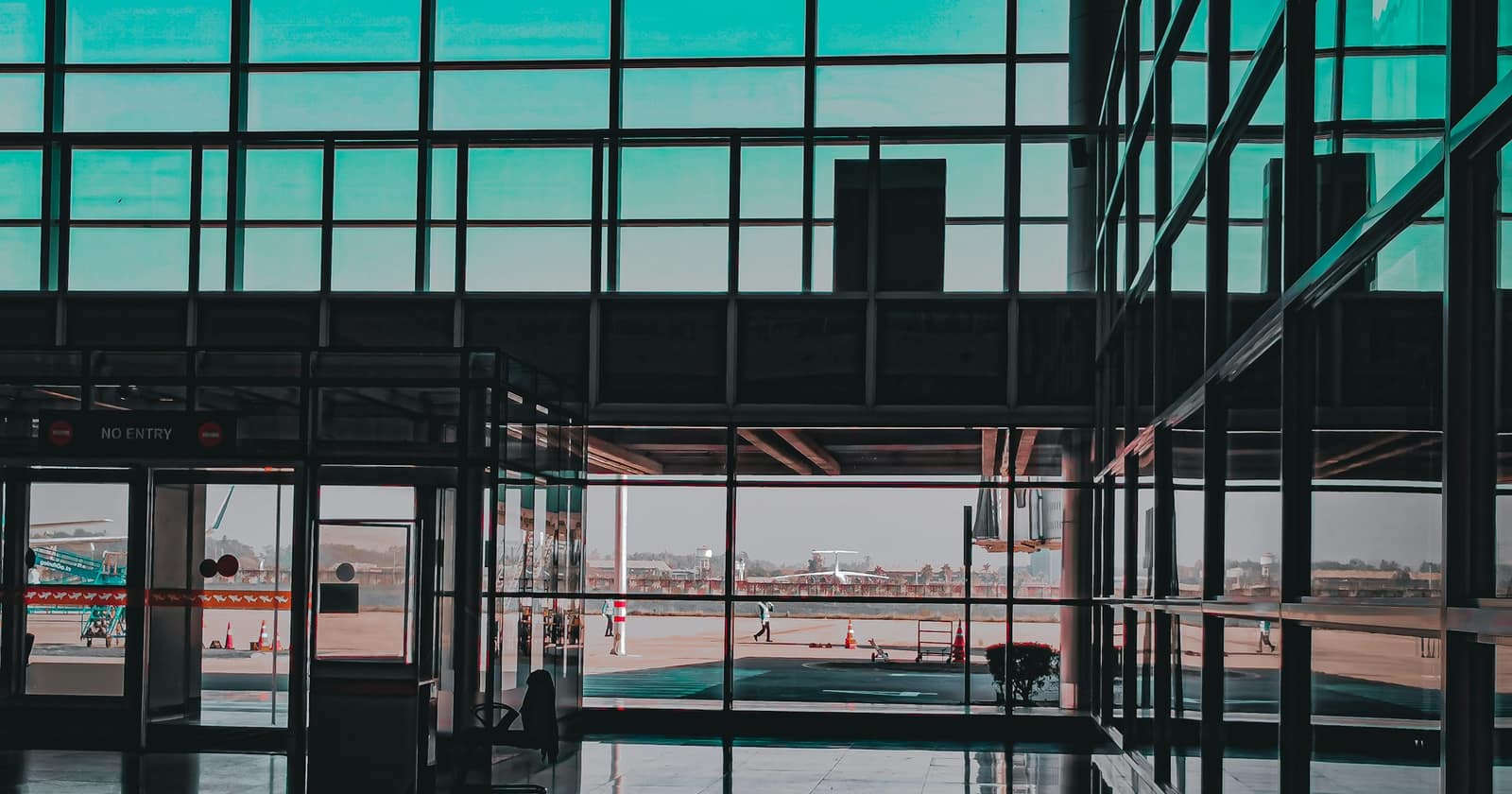 An airport terminal's glass wall in silhouette, looking out across the apron to a waiting aircraft