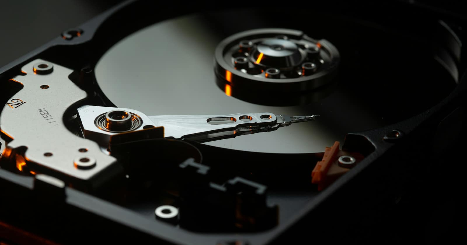 The platter and read arm of an opened hard disk drive, lit in amber against a dark background