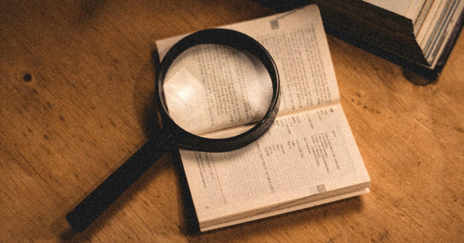 A magnifying glass resting on an open book on a wooden desk