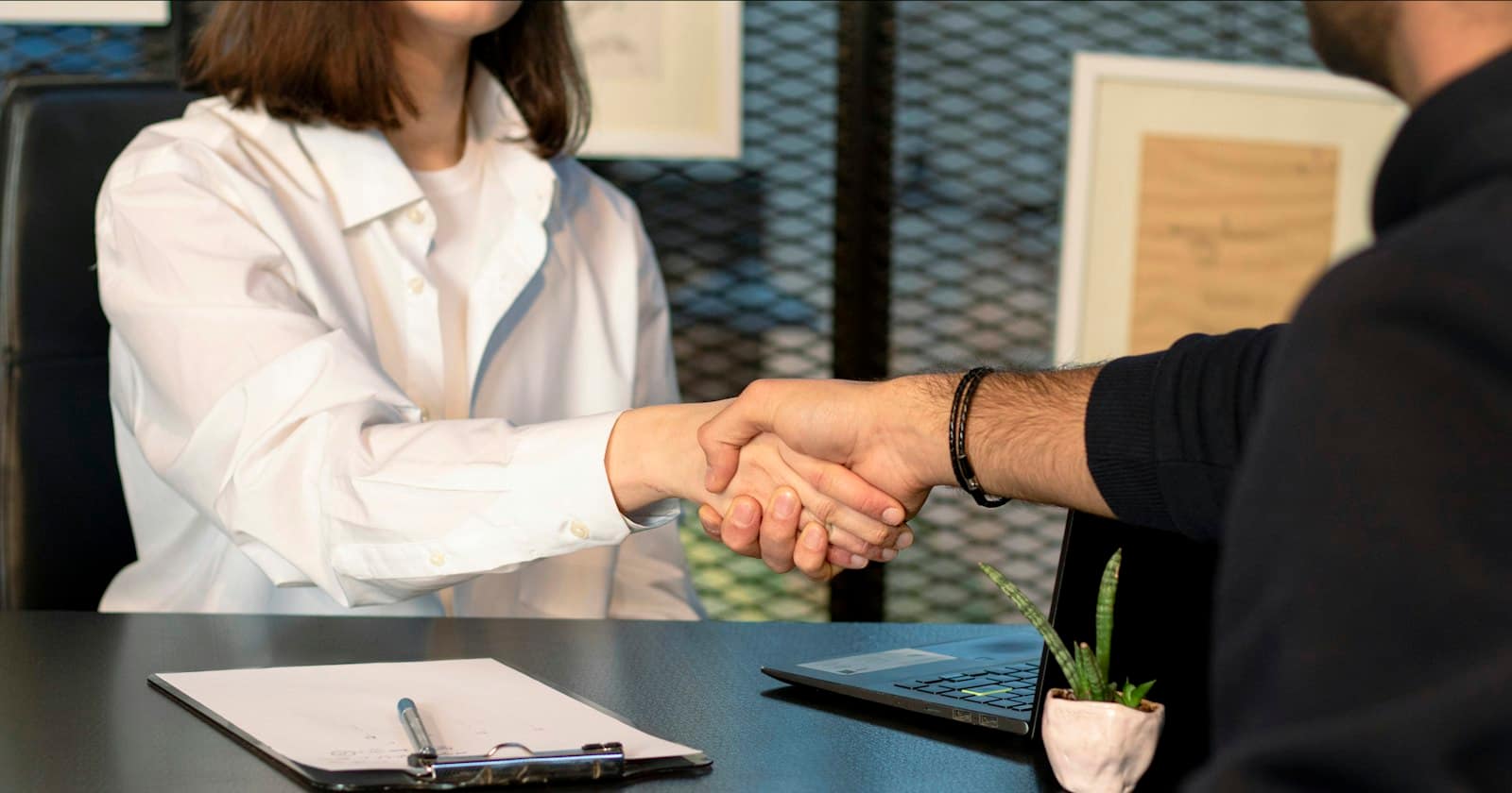 Two partners shaking hands across an office desk