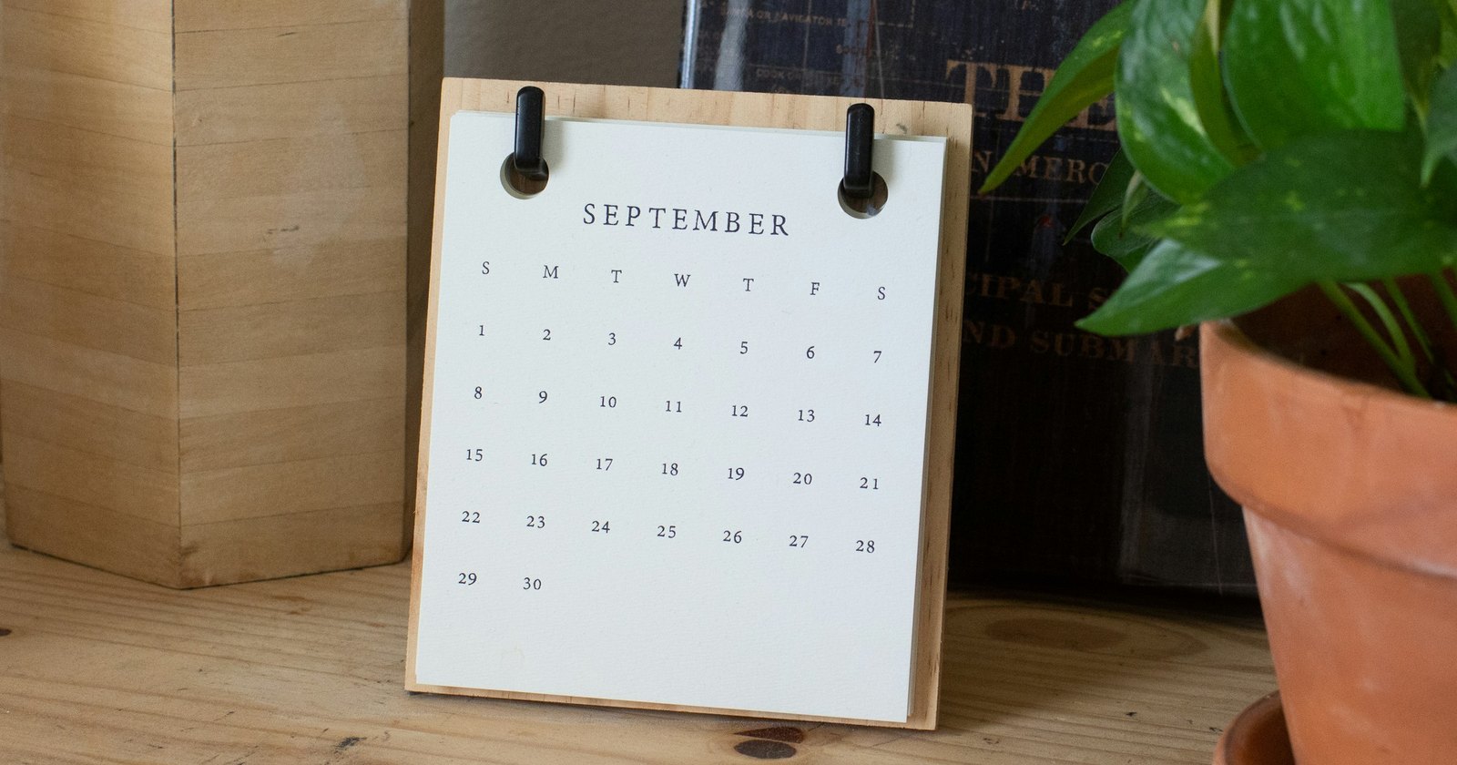 A September desk calendar on a wooden stand beside a potted plant