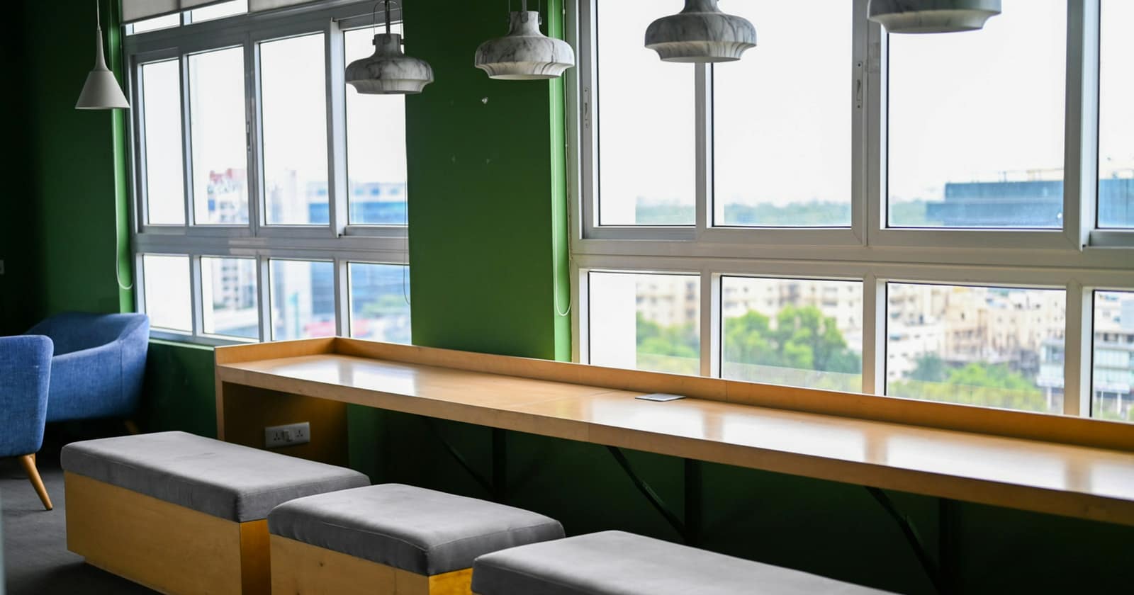 Benches and a long wooden desk under pendant lamps by the windows of a Bengaluru start-up office