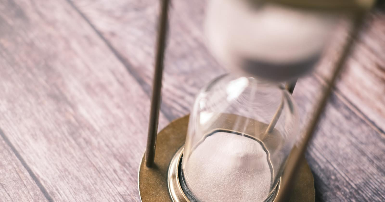 The last grains of sand settling in the lower bulb of a brass hourglass on a wooden table