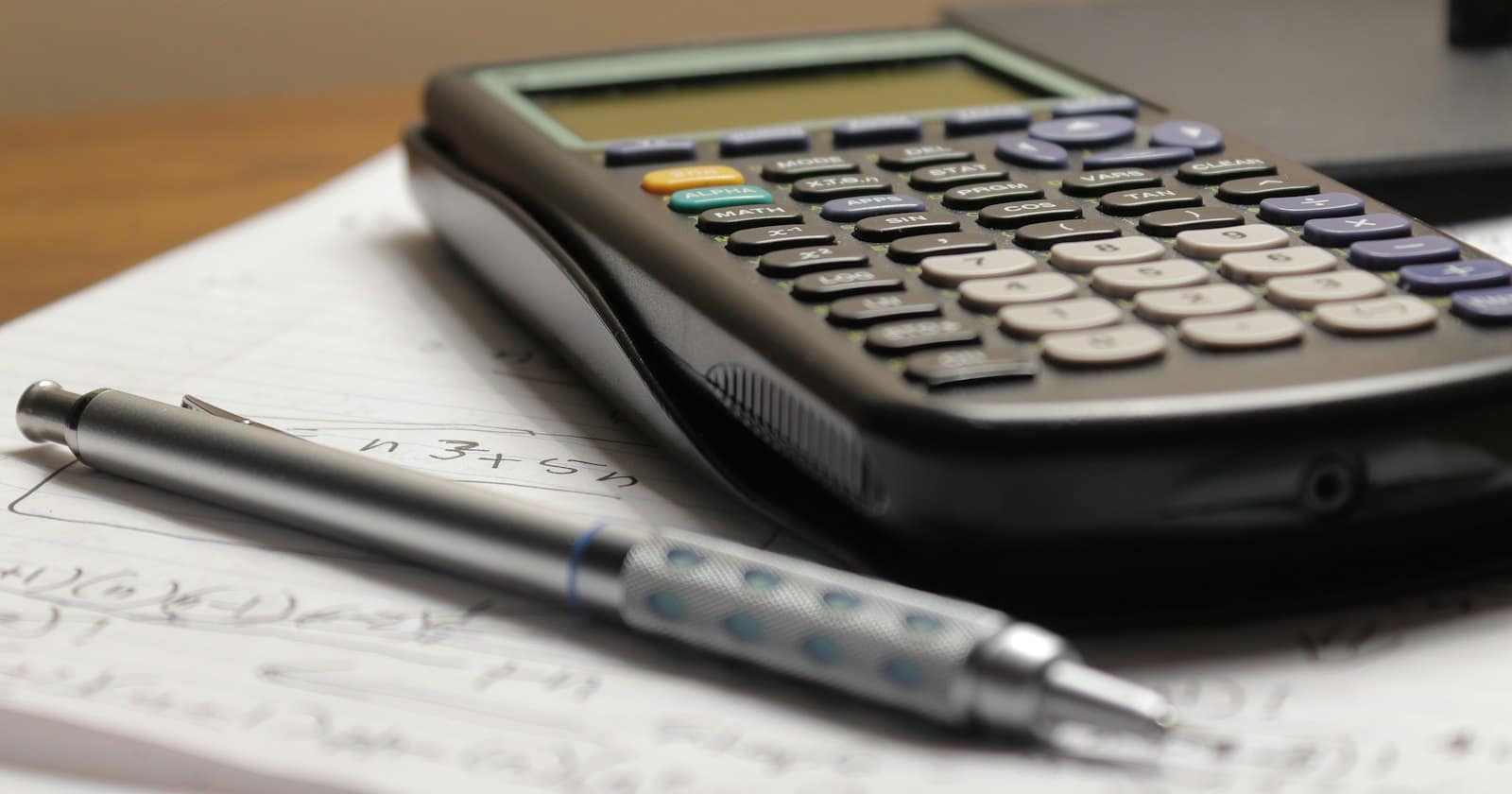 A calculator and a pen resting on a sheet of handwritten working