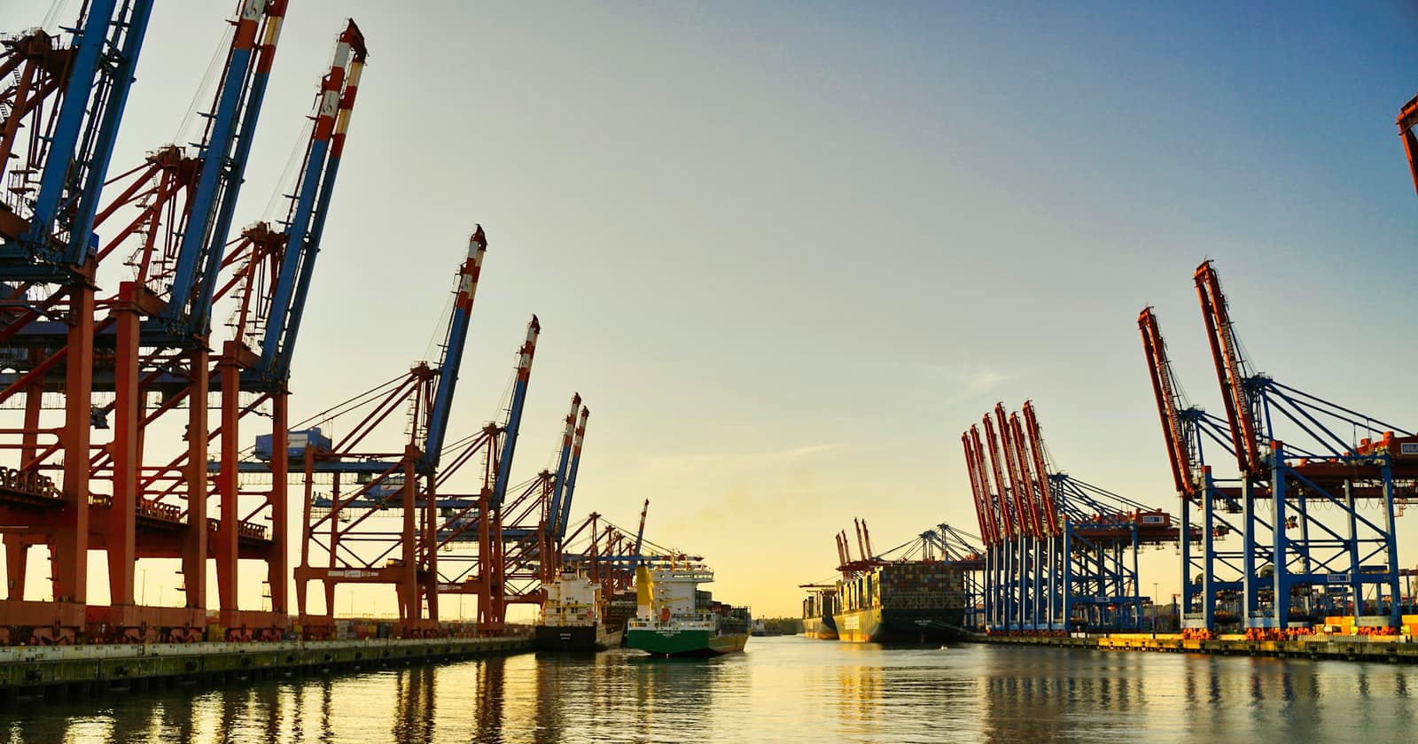 Rows of container cranes along a harbour at dusk, with a ship alongside